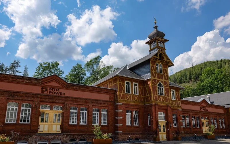 Das historische MTM-Power-Werksgebäude im Schwarzatal: Backsteinfassade mit gelbem Fachwerkturm und Zwiebelhaube, dahinter ein bewaldeter Hang